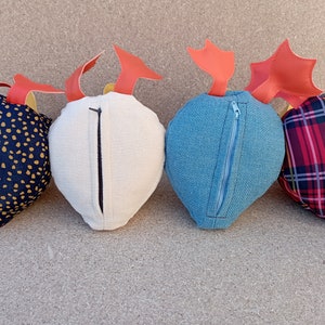 May include: Four plush heart-shaped pillows with different fabric patterns. Each pillow has a zipper closure and a red felt accent on top.
