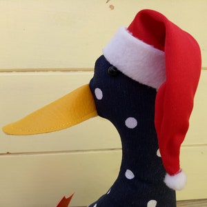 May include: A black and white polka dot duck wearing a red Santa hat with a white trim. The duck has a yellow beak and black eyes.