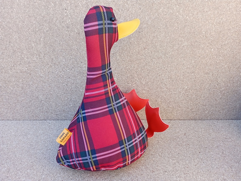 May include: Red and black plaid duck plush toy with a yellow beak and red wings. The toy has a label that says "Cool Canard".