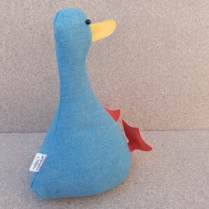 May include: A blue fabric duck with a yellow beak and red wings. The duck is a stuffed toy and has a small label on the side that says "Doodle  Cavalier".