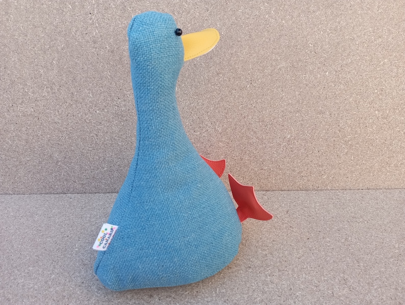 May include: A blue fabric duck with a yellow beak and red wings. The duck is a stuffed toy and has a small label on the side that says "Doodle  Cavalier".