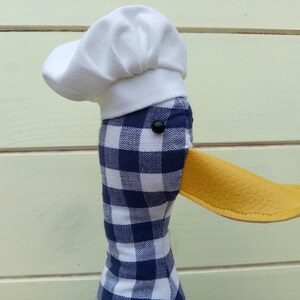 May include: A blue and white checkered fabric duck with a white chef's hat and a yellow leather beak.