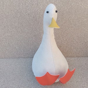 May include: White plush goose doorstop with orange feet and a yellow beak.