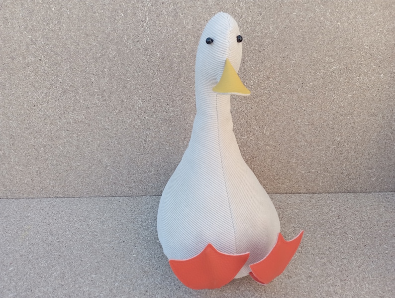 May include: White plush goose doorstop with orange feet and a yellow beak.
