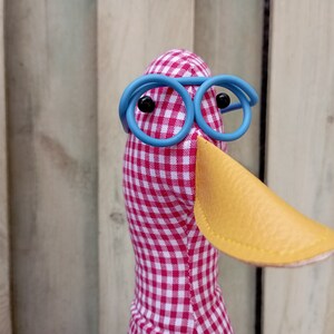 May include: A red and white checkered fabric duck with a yellow beak and blue round glasses.