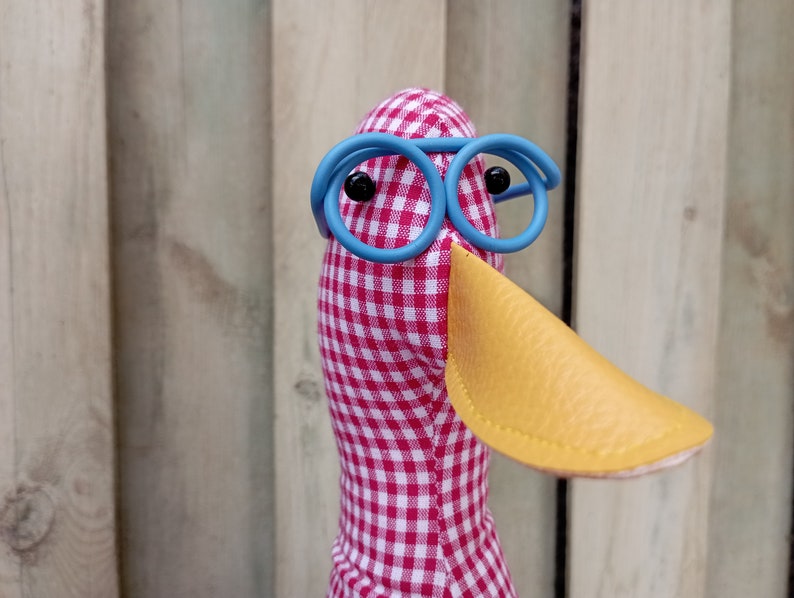 May include: A red and white checkered fabric duck with a yellow beak and blue round glasses.