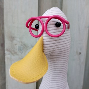 May include: A white stuffed duck with a yellow beak and pink round glasses.