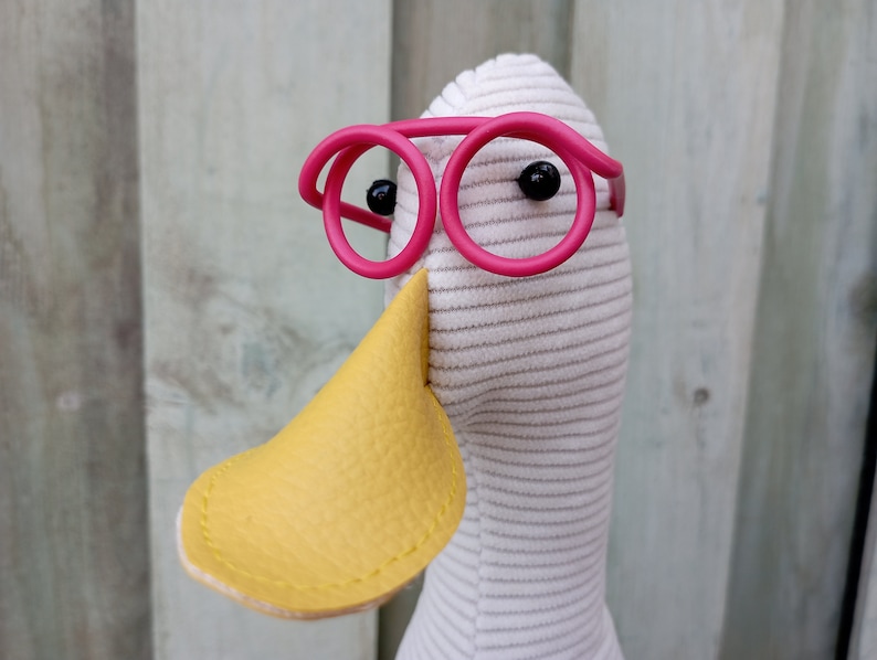 May include: A white stuffed duck with a yellow beak and pink round glasses.