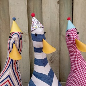 May include: Three plush toy ducks wearing party hats. The ducks are striped in red and white, blue and white, and red and white gingham.