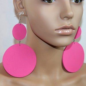 May include: A pair of large, pink, round wooden earrings. The earrings are dangling and have a silver hook.