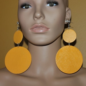 May include: A pair of large, round, mustard yellow earrings. Each earring has two circles, one smaller than the other, connected by a silver chain.