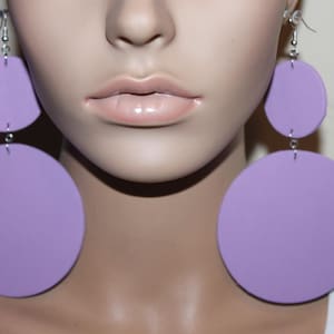 Op de afbeelding: Een paar grote, lavendelkleurige schijfoorbellen. Elke oorbel heeft twee verbonden cirkels, een kleinere boven een grotere. De oorbellen hangen aan zilverkleurige haken. De oorbellen zijn een gedurfde mode-uitspraak.