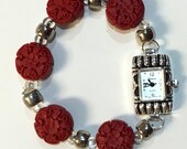 Brighton-inspired Classic, modern, retro. Red carved cinnabar, silver-plated watch face, metal and silver-lined glass beads. Stretch band.