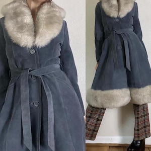 May include: A slate blue suede coat with a faux fur collar and cuffs. The coat features a belted waist and button closures. The coat is knee-length and has a flared skirt.
