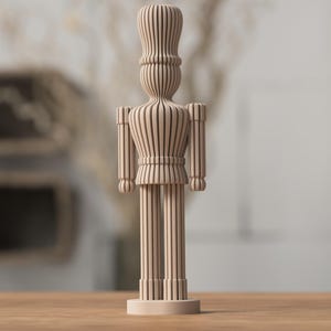 Puede incluir: Figura de cascanueces de madera de color marrón claro. La figura tiene una cabeza alta y cilíndrica, un torso detallado y piernas largas. El diseño presenta ranuras verticales, lo que le da un aspecto rayado. Se apoya sobre una base pequeña y redonda.