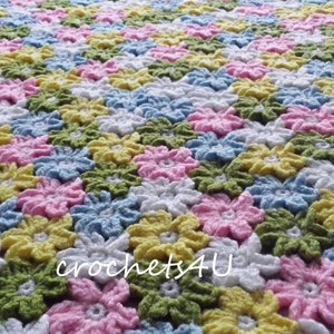May include: A crocheted baby blanket with a floral pattern in shades of pink, yellow, green, blue, and white. The blanket is made with a repeating flower design.