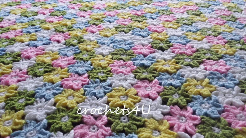May include: A crocheted baby blanket with a floral pattern in shades of pink, yellow, green, blue, and white. The blanket is made with a repeating flower design.