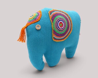 Op de afbeelding: Een felblauw gehaakt olifantenspeeltje met een groot, meerkleurig cirkelvormig patroon op de zijkant en een kleinere bijpassende cirkel op de kop. Het heeft een lichtbruine ronde knoop als oog en een feloranje kwastje van garen als staart.
