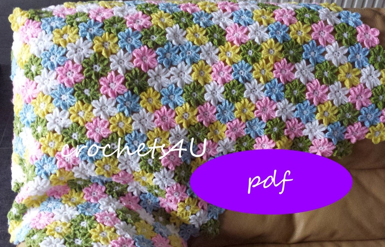 May include: A crocheted baby blanket with a flower pattern in shades of pink, blue, yellow, green, and white. The blanket is made with a simple stitch and has a soft, fluffy texture. The text "crochets4U pdf" is visible in the image.