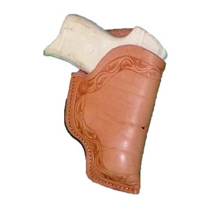 Può includere: Un fodero in pelle marrone con un intricato disegno floreale. Una pistola di plastica bianca è all'interno del fodero.
