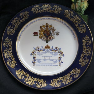 Può includere: Un piatto commemorativo con bordo blu navy e design a filigrana dorata. Il centro presenta uno stemma reale e un testo che commemora il matrimonio del Principe di Galles con Lady Diana Spencer. Il piatto misura circa 25 cm di diametro.
