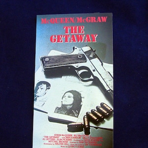 以下が含まれることがあります： スティーブ・マックイーンとアリ・マッグロー主演の映画「ゲットアウェイ」の映画ポスター。ポスターには、銃、弾丸、俳優の顔写真が写っている。