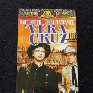 May include: A DVD cover for the movie "Vera Cruz" starring Gary Cooper and Burt Lancaster. The cover features a dramatic image of the two actors in their Western attire, standing against a backdrop of a sunset and a town.