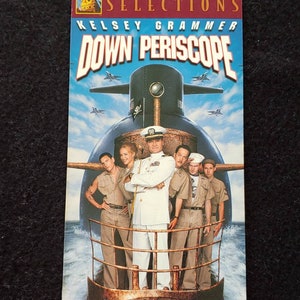 Puede incluir: Una carátula de cinta VHS para la película "Down Periscope" protagonizada por Kelsey Grammer. La carátula presenta un submarino con una calavera y huesos cruzados en el lateral y un grupo de hombres de pie en la cubierta.