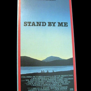 May include: A VHS video cassette cover for the movie "Stand By Me" featuring a scenic landscape with a lake and mountains in the background. The cover features the title "Stand By Me" in large, bold letters and a list of the actors and production company.