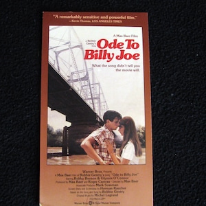 May include: Movie poster for the film "Ode to Billy Joe" starring Robby Benson and Glynnis O'Connor. The poster features a couple standing on a bridge over a river. The text "What the song didn't tell you the movie will." is printed on the poster.