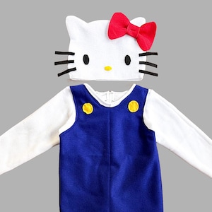 Peut inclure: Un costume Hello Kitty blanc pour bébé ou tout-petit. Le costume comprend une combinaison blanche avec une salopette bleue et des boutons jaunes, et un chapeau Hello Kitty blanc avec un nœud rouge.
