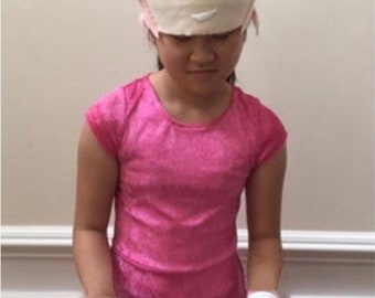 May include: A young person wearing a pink and white costume with a pink and white hat featuring a cartoon character with green eyes. The costume includes a pink dress and white gloves.