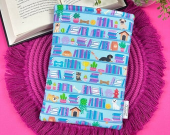 May include: A blue book sleeve with a pattern of books, dogs, and other dog-related items. The text "Woof" is printed on the sleeve. The sleeve is on a pink fringed surface.