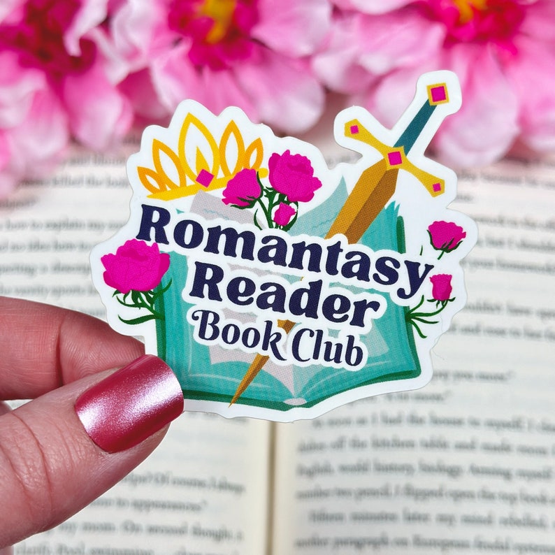 May include: A sticker with a book, a crown, flowers, and a sword. The text on the sticker reads "Romantasy Reader Book Club".