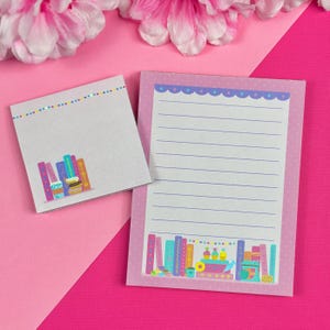 May include: Two pink and white notepad sets with lined paper. One notepad has a colourful illustration of books and a cup of coffee. The other notepad has a colourful illustration of books, cupcakes, and a teacup.