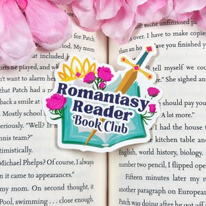 May include: A sticker with a blue book, a sword, and pink flowers. The text on the sticker reads "Romantasy Reader Book Club".