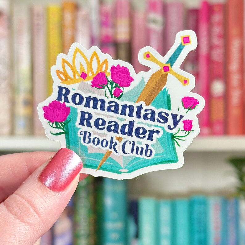 May include: A white sticker with a blue and green book, a gold crown, a sword, and pink flowers. The text on the sticker reads "Romantasy Reader Book Club".