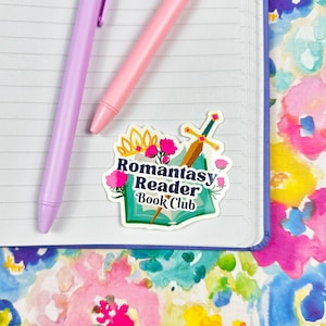 May include: A sticker with a whimsical design featuring a book, a sword, flowers, and a crown. The text reads "Romantasy Reader Book Club".