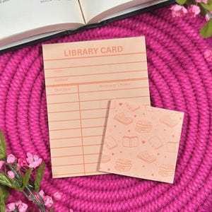 May include: Peach-coloured library card and matching square card with a book pattern. The library card has lines for title, author, due date, and borrower's name. The text "LIBRARY CARD" is printed at the top.