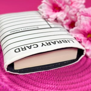 Foam padded book cover laying flat with a book inside.  The book sleeve has a design made to look like a library card.  It is great to take to book signings and events to collect author signatures.