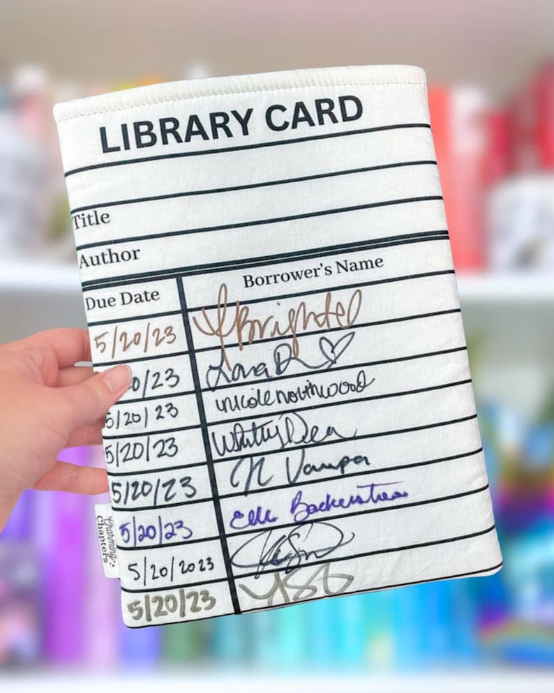 May include: A white library card sleeve with black lines and text. The text "LIBRARY CARD" is at the top. The sleeve has sections for title, author, due date, and borrower's name. Handwritten names and dates fill the spaces.
