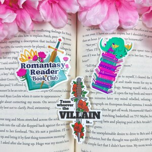 May include: Four colorful stickers featuring book-themed illustrations. The first sticker features a sword and roses with the text "Team whoever the VILLAIN is..." The second sticker features a dragon reading a stack of books. The third sticker features a stack of books with the text "Romantasy Reader Book Club". The fourth sticker features a sword and roses with the text "Team whoever the VILLAIN is..."