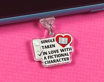 May include: A clear acrylic keychain with a red heart and a book inside. The keychain has a checklist with the options "Single", "Taken", and "In love with a fictional character". The "In love with a fictional character" option is checked.