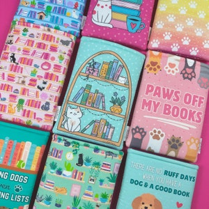 Peut inclure: Plusieurs prot&egrave;ge-livres avec des motifs vari&eacute;s. Certains pr&eacute;sentent des chats, des &eacute;tag&egrave;res et des empreintes de pattes. L'un d'eux porte l'inscription "PAWS OFF MY BOOKS". Un autre dit "THERE ARE NO RUFF DAYS WHEN YOU HAVE A DOG & A GOOD BOOK".