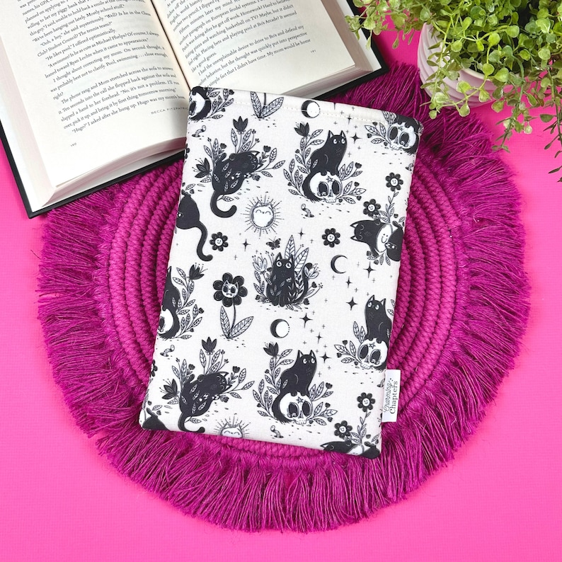 May include: A white book cover with a black and white illustration of cats, flowers, and moons. The book cover has the text 'Grammarly Chapters' on the bottom right corner.
