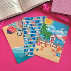 May include: Three colorful rectangular bookmarks with beach-themed illustrations. One shows a beach scene with a lifeguard stand, palm trees, and seagulls. Another depicts a bookshelf with beach-related items. The third shows a beach with books.