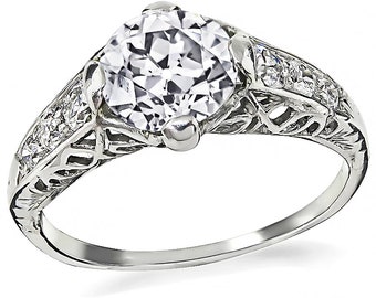 May include: A vintage-style engagement ring with a large, round, clear center stone and smaller, clear stones set in a filigree band.