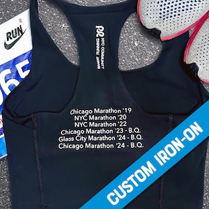 May include: Black sports bra with white text on the back, listing various marathons and the text "CUSTOM IRON-ON".