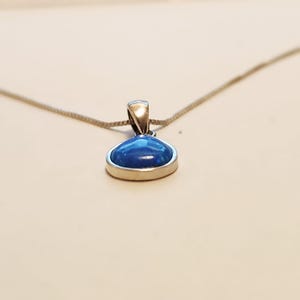 Peut inclure: Un collier en argent avec un pendentif. Le pendentif est orné d'une pierre précieuse ovale bleue vive sertie dans une lunette en argent. La chaîne est une fine chaîne en argent. La pierre a une finition brillante.