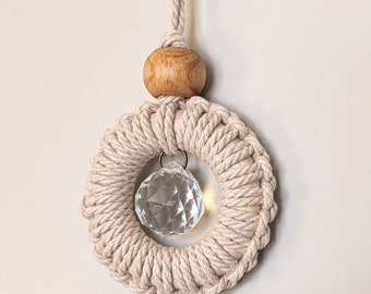 May include: A beige macrame circle with a crystal prism hanging in the center. The circle is attached to a wooden bead and a beige cord.